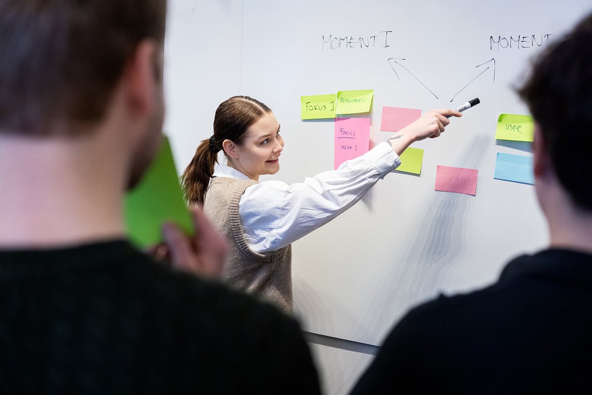 woman points with pen to whiteboard
