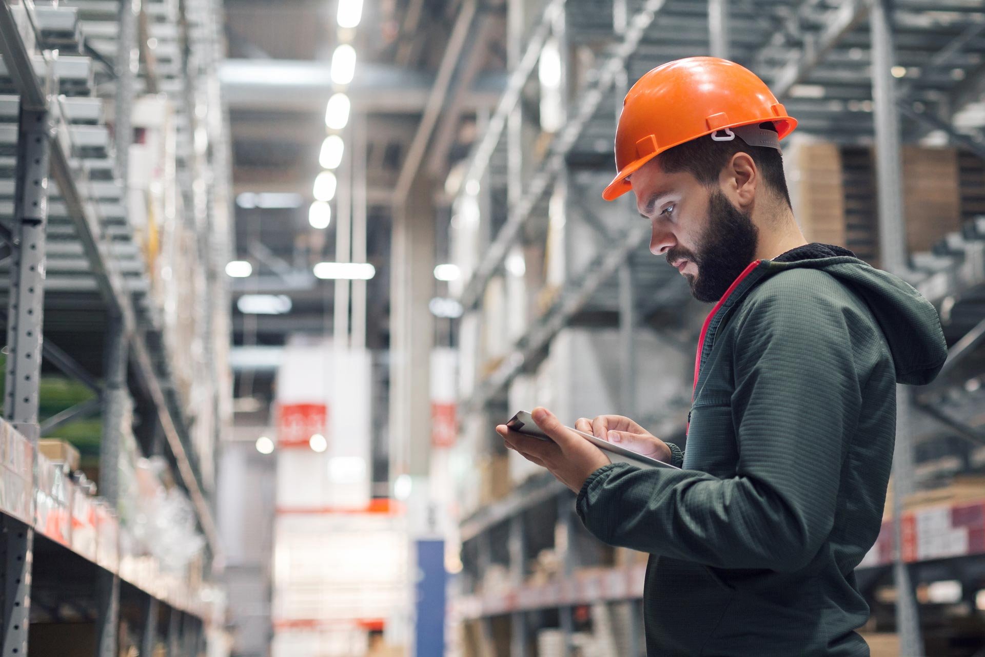 Man with orange helmet and reading tablet in a warehouse